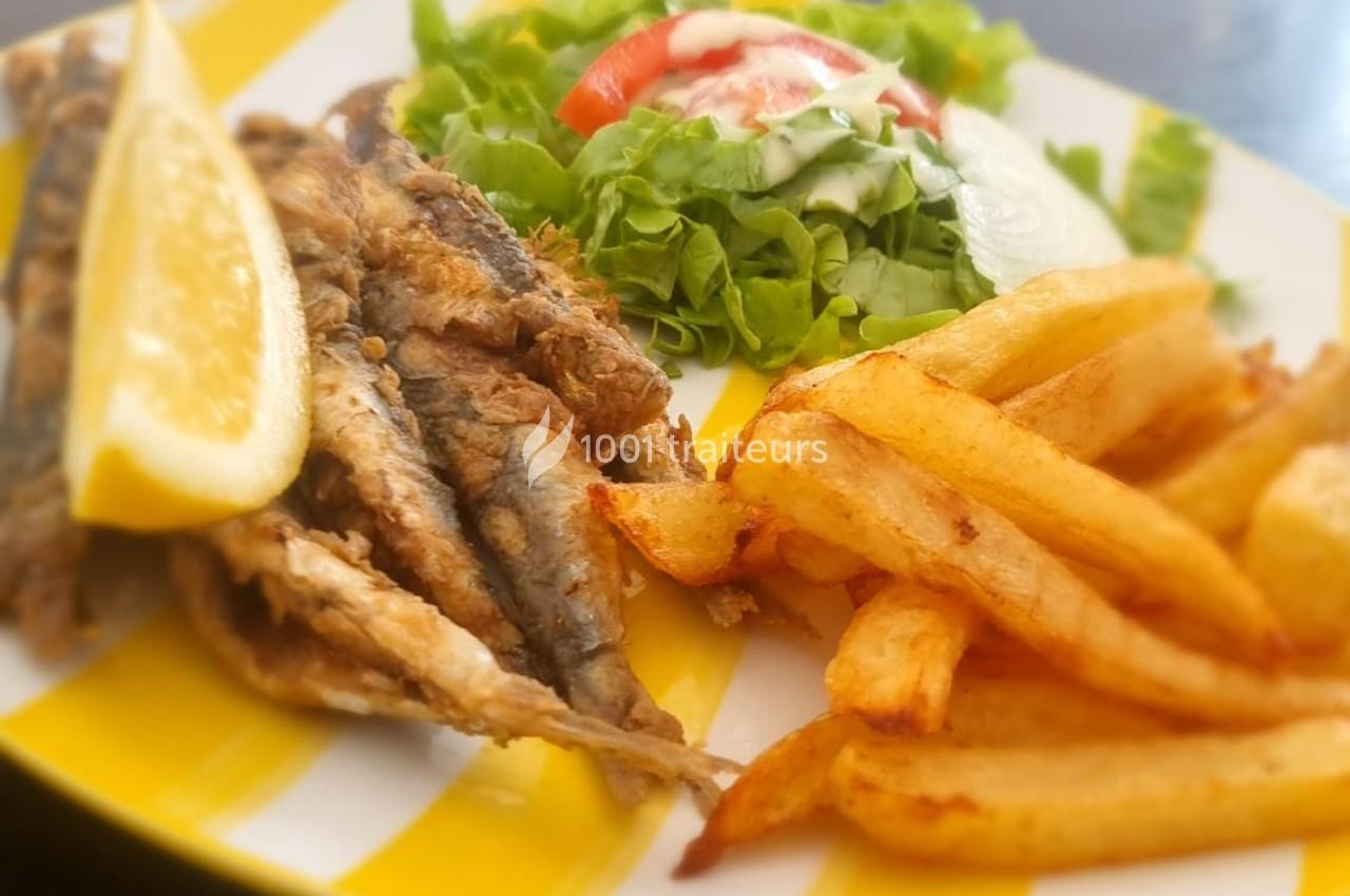 Assiette contenant des sardines grillées, des frites dorées, une tranche de citron et une salade verte avec tomate.