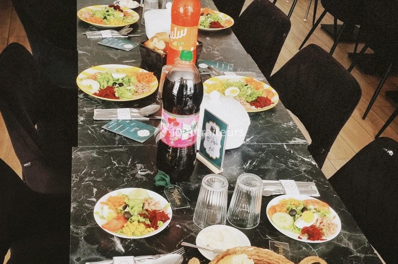 Table dressée avec des assiettes de salades variées, boissons, couverts et serviettes sur une nappe noire.