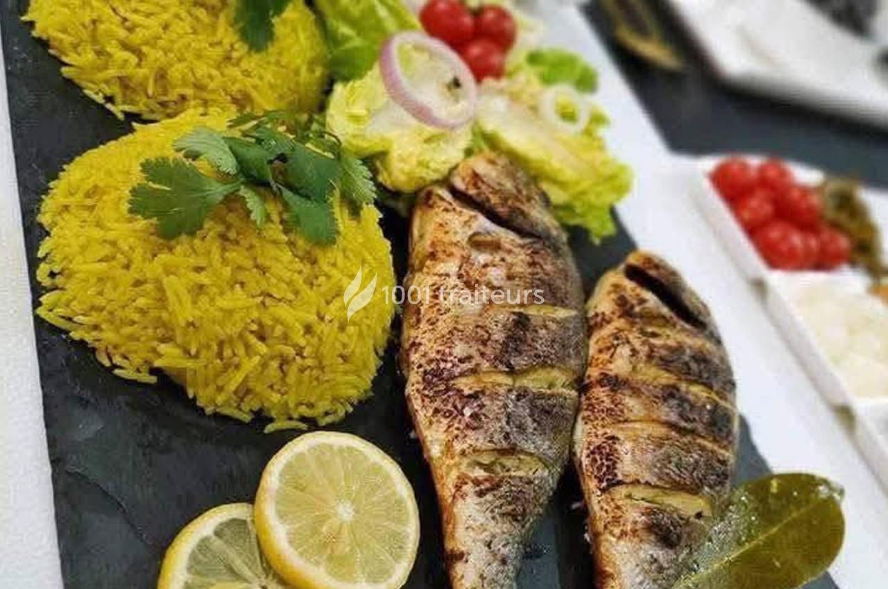 Deux poissons grillés servis avec du riz jaune, des rondelles de citron, de la salade et des légumes frais.