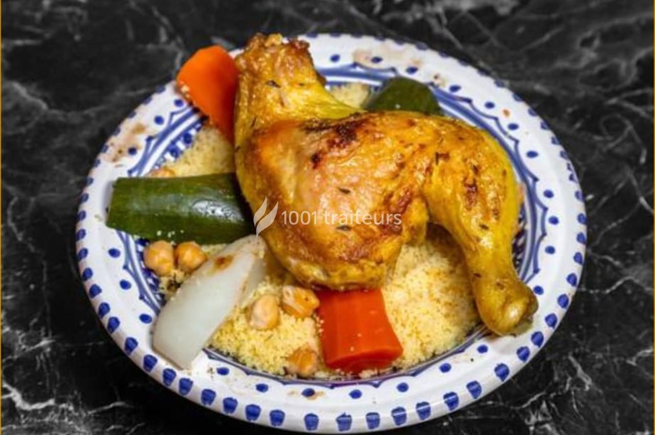 Assiette de couscous garnie d'une cuisse de poulet rôti, légumes variés et pois chiches sur une table en marbre noir.