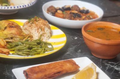 Bol de soupe garnie de coriandre sur une table en marbre avec des couverts, des verres et une salière en arrière-plan.