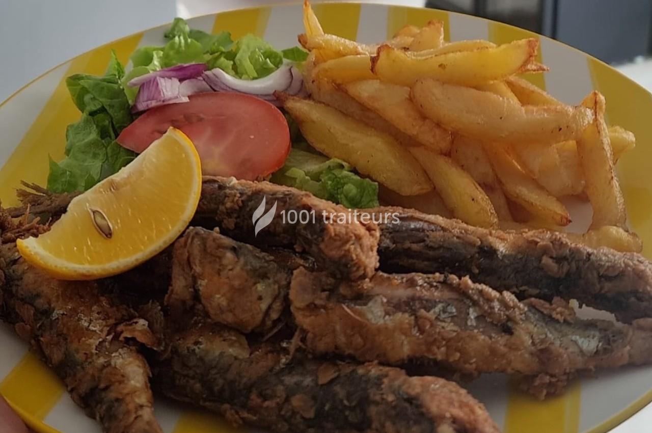 Assiette contenant des sardines frites, des frites dorées, une salade verte, une tranche de tomate et un quartier de citron.
