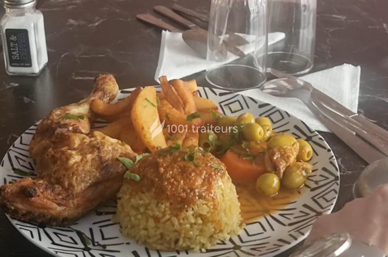 Assiette composée de poulet rôti, riz épicé, légumes en sauce avec olives, et frites, sur une table dressée.