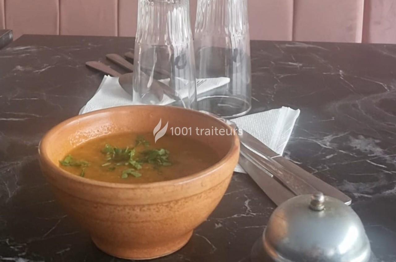 Bol de soupe garnie de coriandre sur une table en marbre avec des couverts, des verres et une salière en arrière-plan.