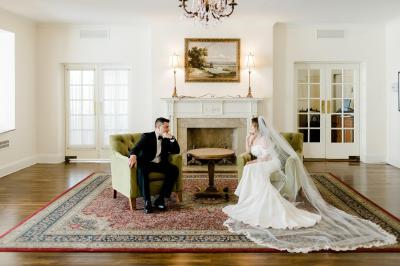 Un couple habillé élégamment se regarde avec tendresse entre deux rideaux blancs.