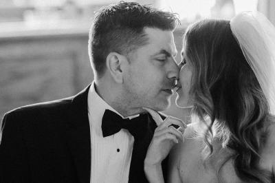 Un couple habillé élégamment se regarde avec tendresse entre deux rideaux blancs.