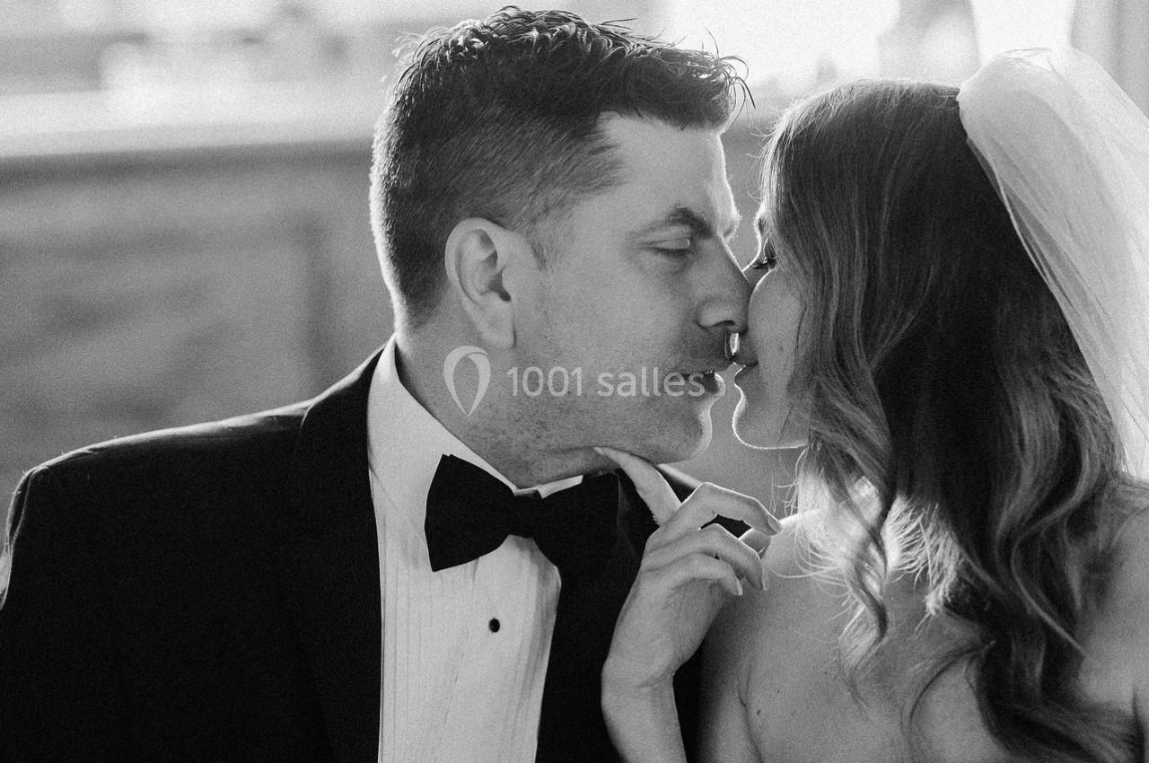 Un couple en tenue de mariage s'apprête à s'embrasser dans une ambiance lumineuse et intime.