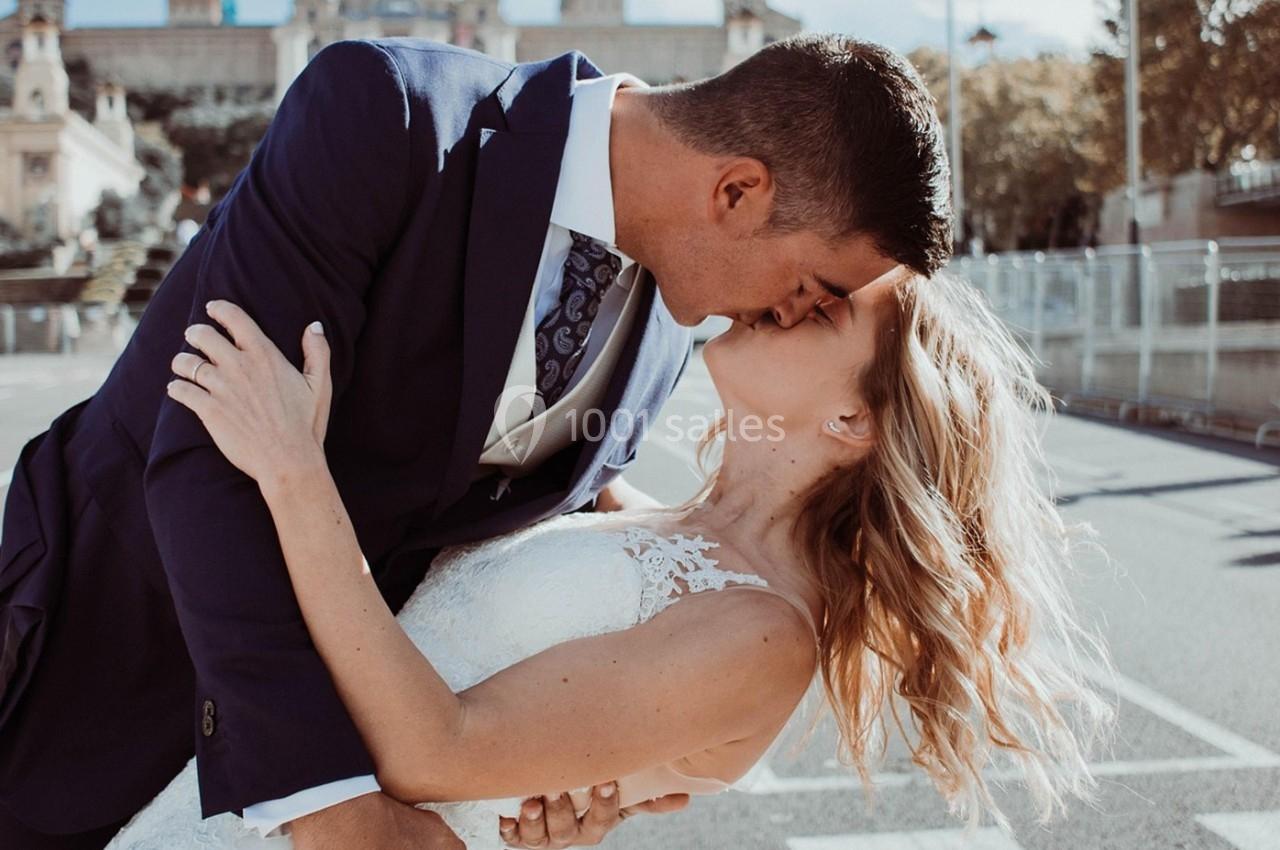 Un couple en tenue de mariage s'embrasse passionnément en extérieur, sous une lumière naturelle.
