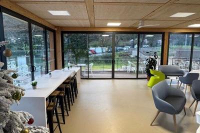 Salle décorée avec des guirlandes colorées et des lanternes, tables dressées pour un événement festif près de grandes baies…