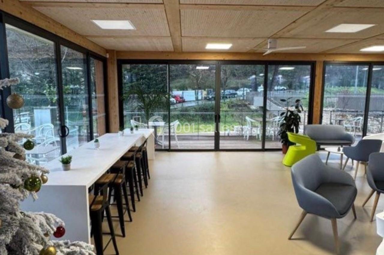 Espace intérieur lumineux avec grandes baies vitrées, tables, chaises modernes et un sapin décoré au premier plan.