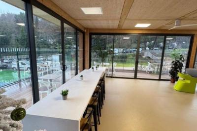 Salle décorée avec des guirlandes colorées et des lanternes, tables dressées pour un événement festif près de grandes baies…