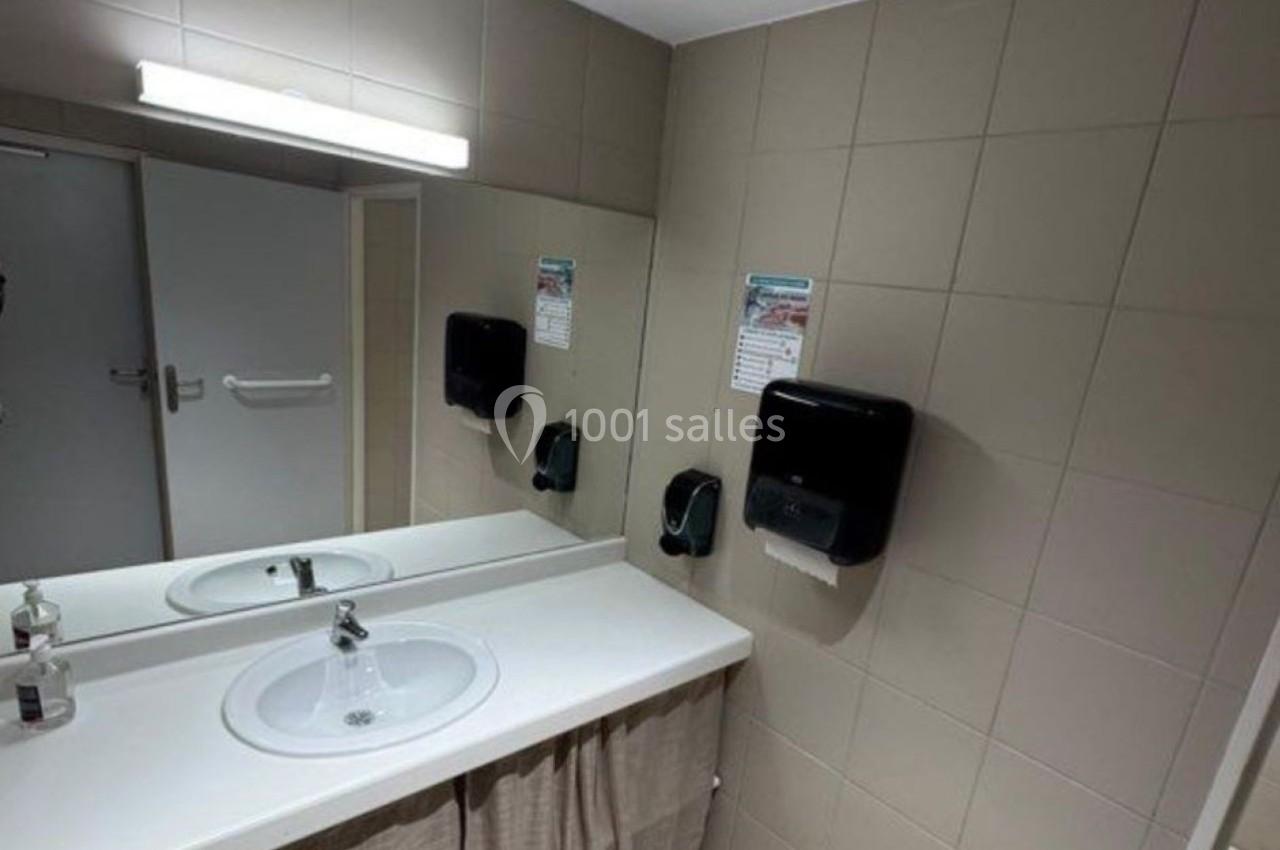 Lavabo double avec miroir dans des toilettes publiques, distributeurs de savon et carrelage beige au mur.