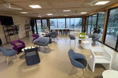 Salle décorée avec des guirlandes colorées et des lanternes, tables dressées pour un événement festif près de grandes baies…