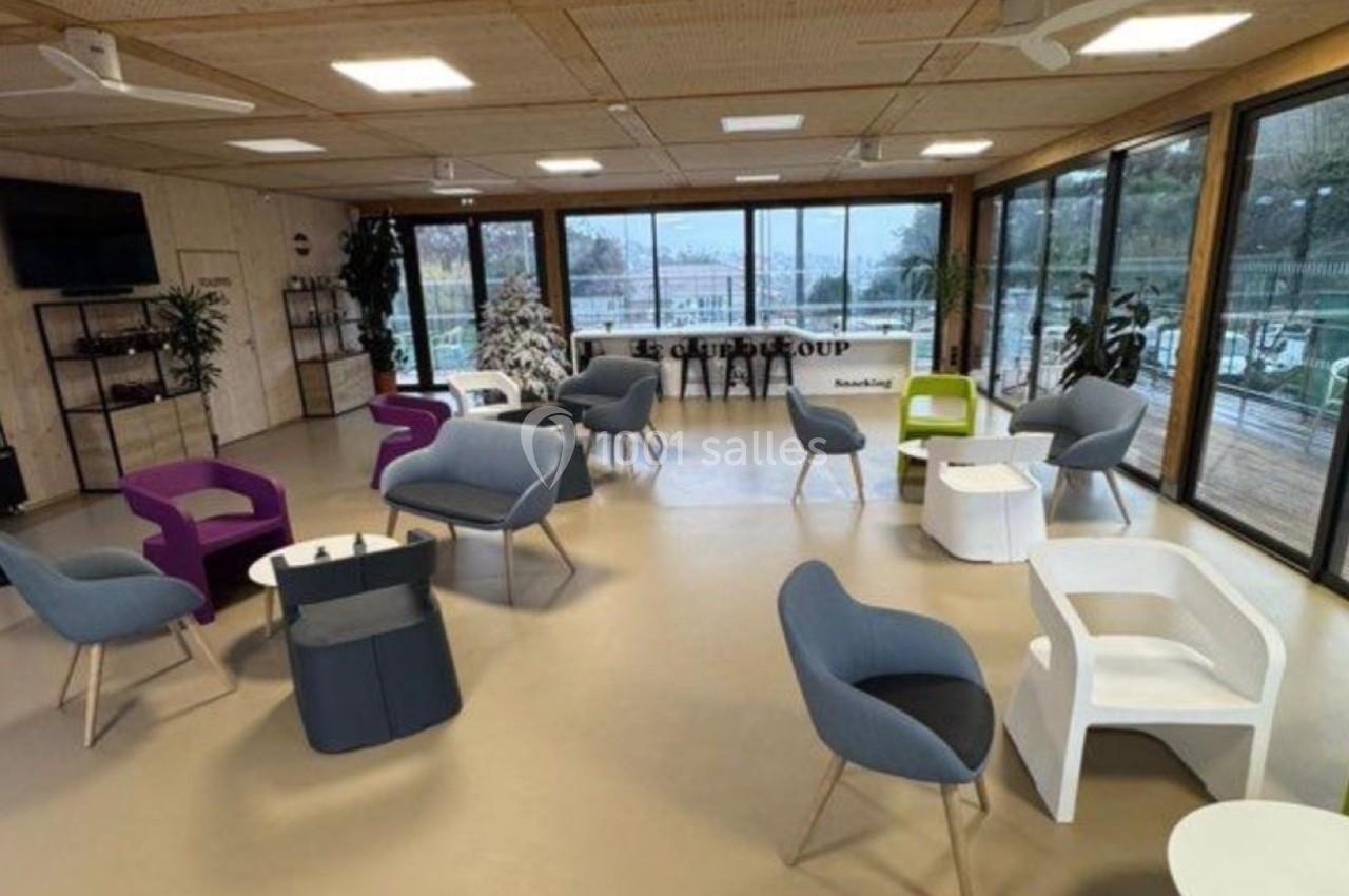 Espace lumineux avec des fauteuils colorés, des tables basses et de grandes baies vitrées donnant sur l'extérieur.