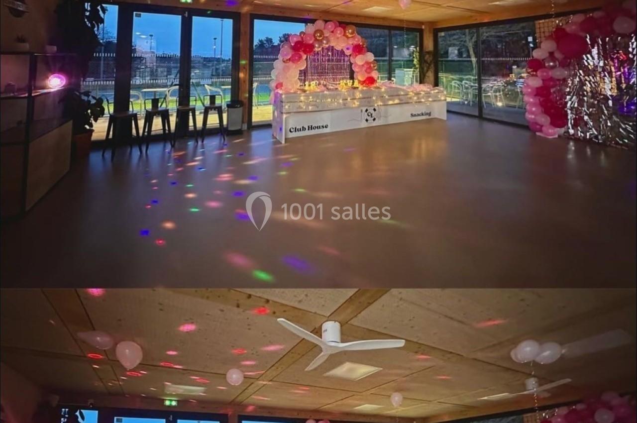 Salle décorée pour un événement avec ballons roses, guirlandes lumineuses et une table ornée au centre.