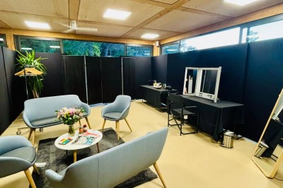 Salle décorée avec des guirlandes colorées et des lanternes, tables dressées pour un événement festif près de grandes baies…