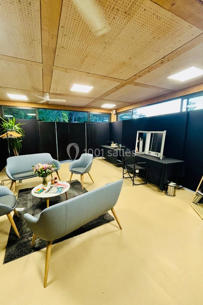 Salle lumineuse avec mobilier moderne, comprenant des fauteuils, une table basse, un miroir et un espace maquillage.