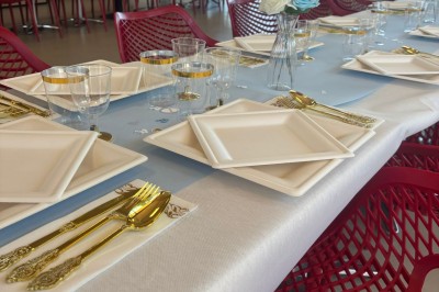 Salle décorée avec des guirlandes colorées et des lanternes, tables dressées pour un événement festif près de grandes baies…
