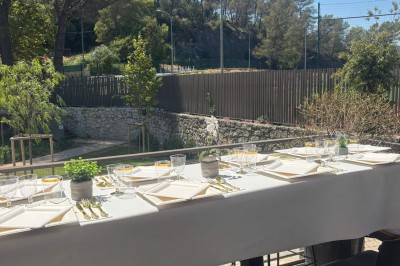 Salle décorée avec des guirlandes colorées et des lanternes, tables dressées pour un événement festif près de grandes baies…