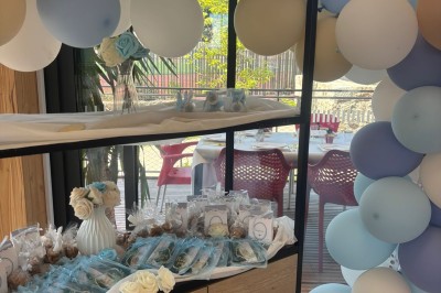 Salle décorée avec des guirlandes colorées et des lanternes, tables dressées pour un événement festif près de grandes baies…