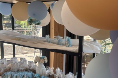 Salle décorée avec des guirlandes colorées et des lanternes, tables dressées pour un événement festif près de grandes baies…