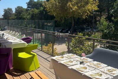 Salle décorée avec des guirlandes colorées et des lanternes, tables dressées pour un événement festif près de grandes baies…