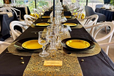 Salle décorée avec des guirlandes colorées et des lanternes, tables dressées pour un événement festif près de grandes baies…