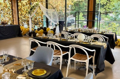 Salle décorée avec des guirlandes colorées et des lanternes, tables dressées pour un événement festif près de grandes baies…