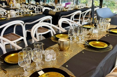 Salle décorée avec des guirlandes colorées et des lanternes, tables dressées pour un événement festif près de grandes baies…