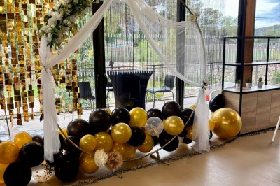 Salle décorée avec des guirlandes colorées et des lanternes, tables dressées pour un événement festif près de grandes baies…