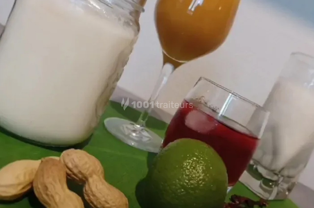 Boissons variées avec cacahuètes, citron vert et fleurs d'hibiscus disposés sur une surface verte.
