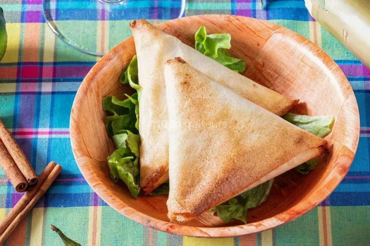 Deux samoussas dorés posés sur des feuilles de salade dans une assiette en bois, sur une nappe colorée.