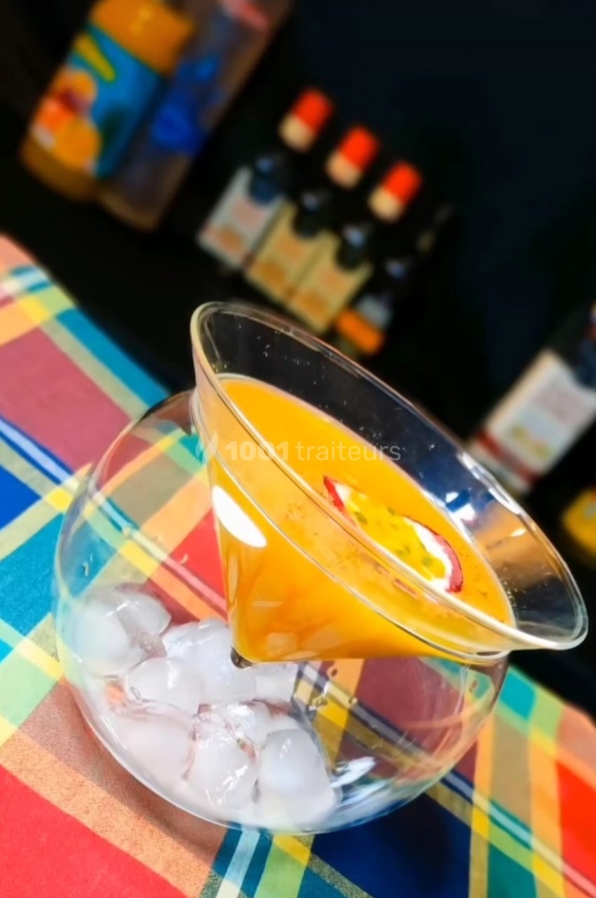 Cocktail orange servi dans un verre conique au-dessus d'un bol rempli de glaçons, sur une nappe colorée.