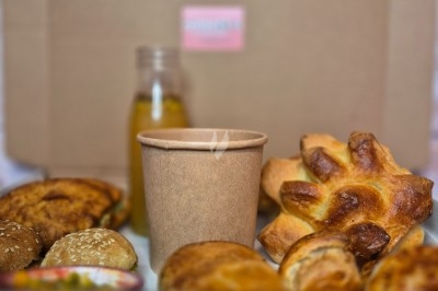 Plateau de viennoiseries, petits pains, fruits de la passion, jus d'orange et boisson chaude dans un gobelet.