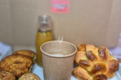 Plateau de viennoiseries, petits pains, fruits de la passion, jus d'orange et boisson chaude dans un gobelet.