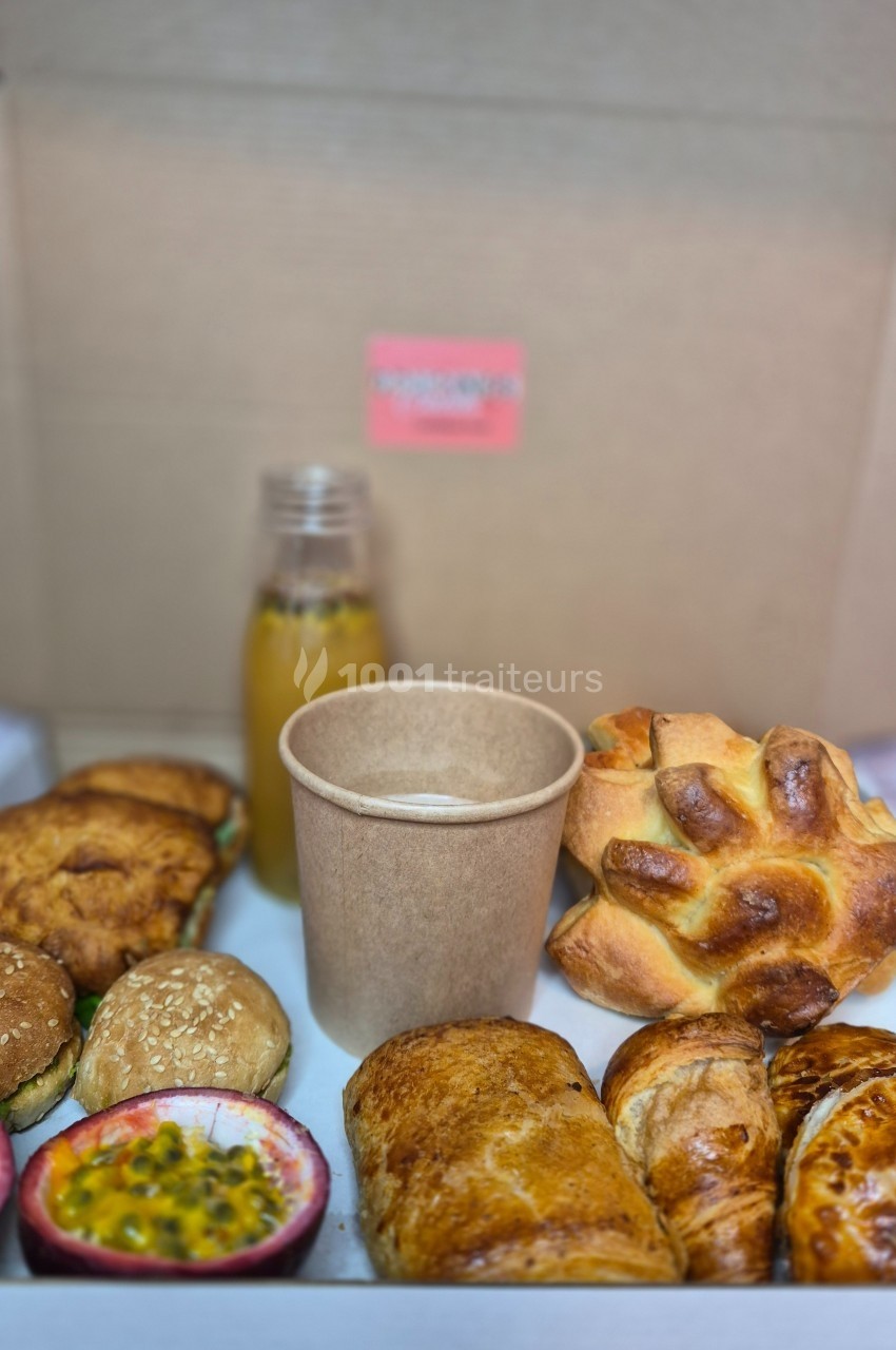 Plateau de viennoiseries, petits pains, fruits de la passion, jus d'orange et boisson chaude dans un gobelet.