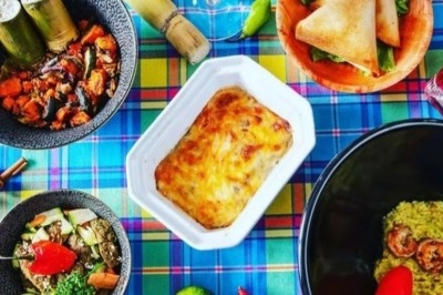Repas coloré composé de plats créoles variés, avec légumes, gratin, samoussas, canne à sucre et piments sur une nappe à…