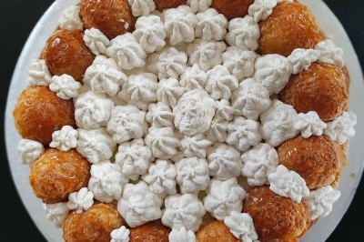 Gâteau composé de choux caramélisés et de crème disposés en cercle sur un fond noir.