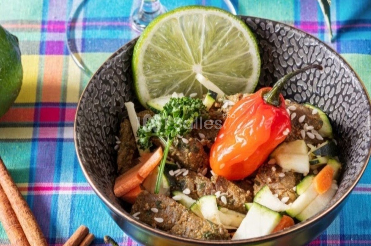 Bol de légumes frais avec citron vert, piment rouge, graines et herbes, sur une nappe colorée à carreaux.