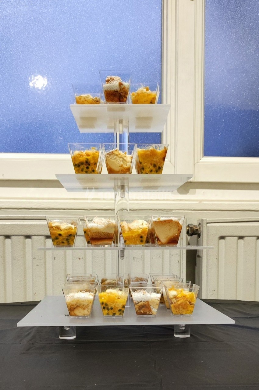 Présentoir à étages avec des verrines de desserts variés, placé devant une fenêtre givrée.