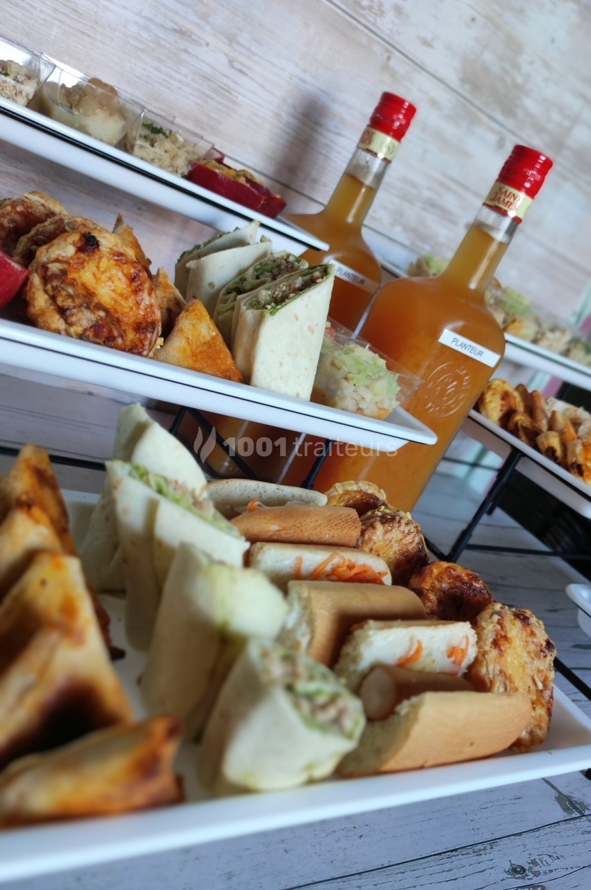 Plateaux garnis de divers amuse-bouches salés et deux bouteilles de sauce sur une table en bois.
