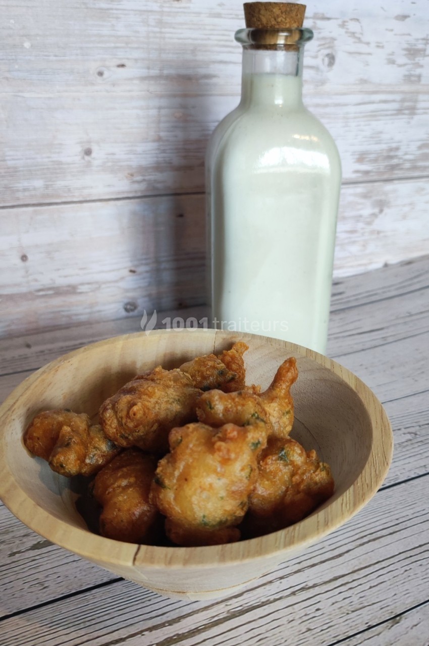 Beignets dorés dans un bol en bois devant une bouteille de verre remplie de liquide blanc, sur une table en bois.