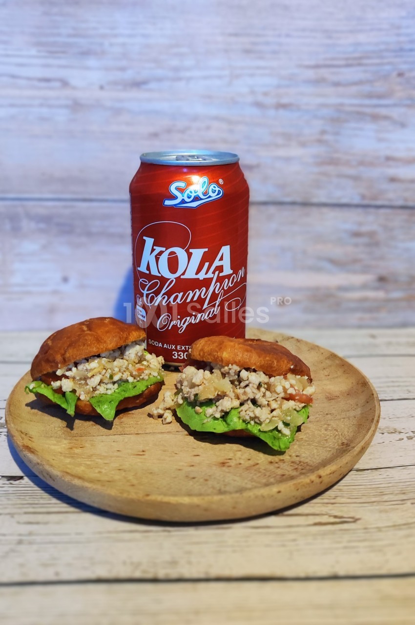 Deux petits sandwichs garnis de salade et de farce, servis sur une assiette en bois avec une canette de soda rouge.