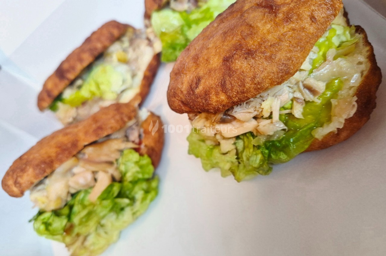 Trois arepas garnis de salade verte, poulet effiloché et légumes, présentés dans une boîte blanche.