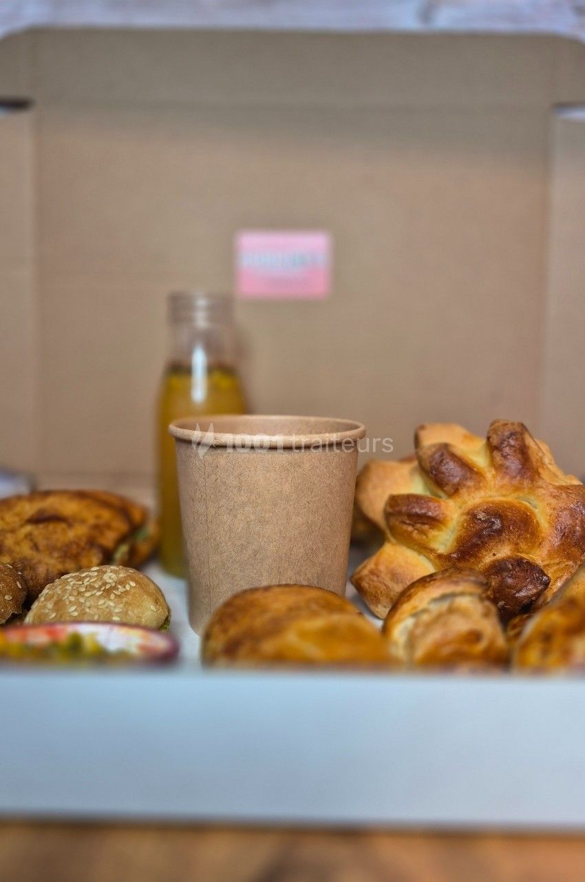 Assortiment de viennoiseries et pain avec une boisson dans un gobelet en carton et une bouteille en arrière-plan.