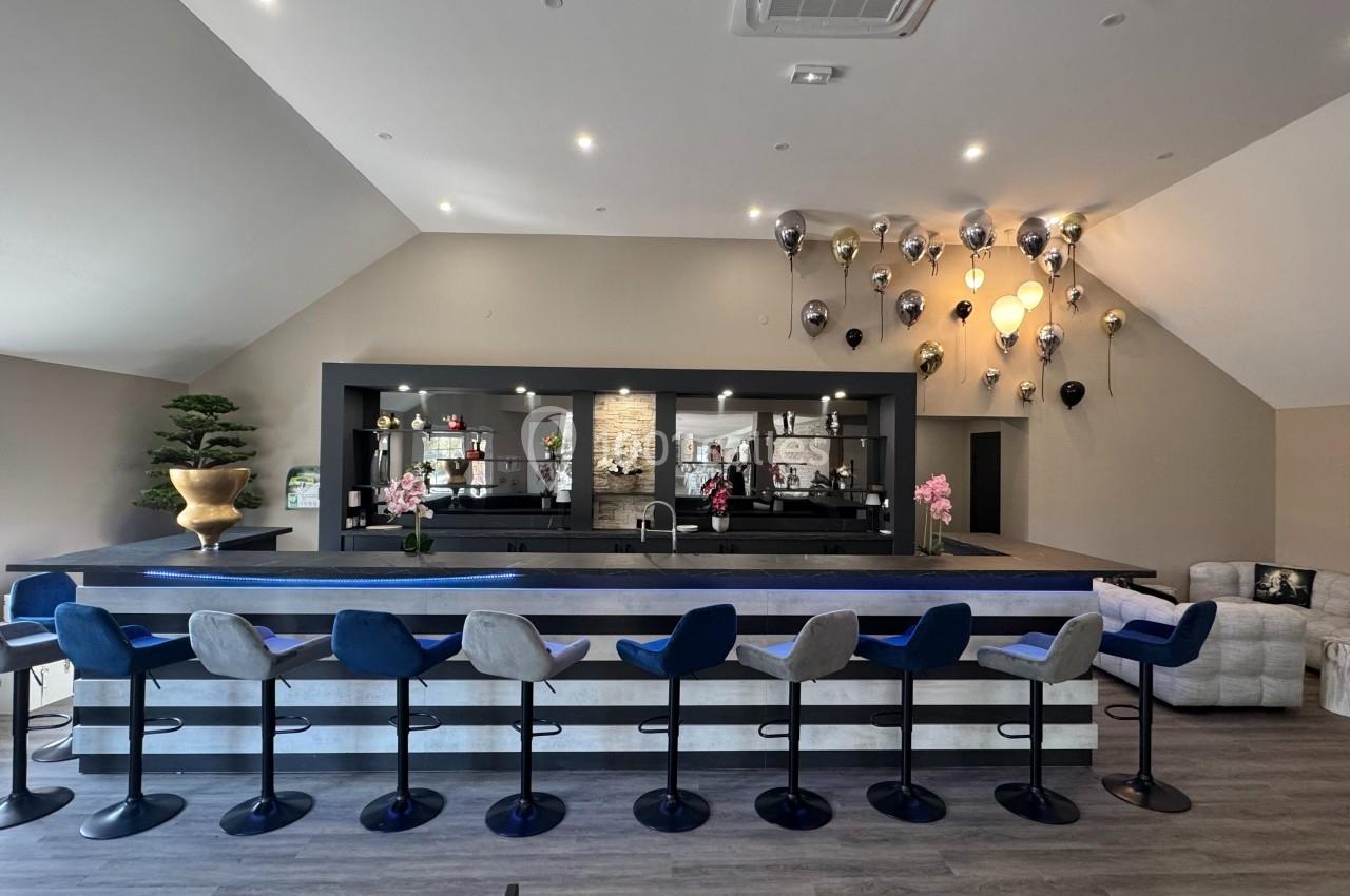 Salle moderne avec un long comptoir, des tabourets alignés, des ballons décoratifs et un espace salon en arrière-plan.