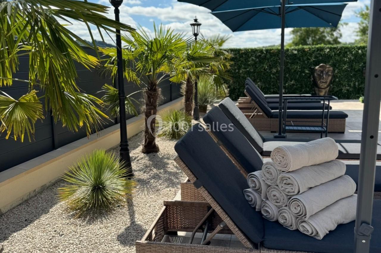 Transats avec serviettes pliées sous des parasols bleus, entourés de plantes et de graviers dans un espace extérieur…