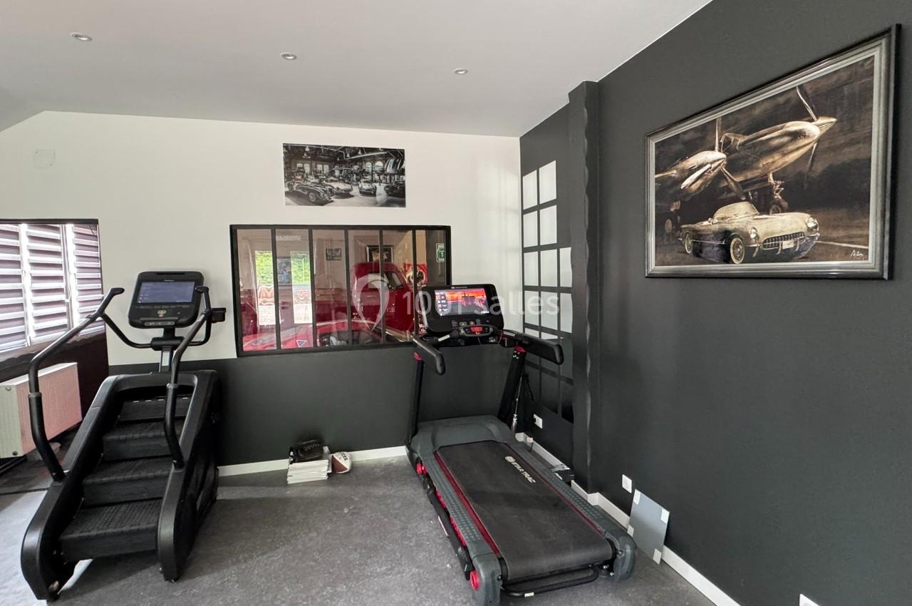 Salle de sport privée avec tapis de course, escalier d'entraînement et décorations murales sur le thème de l'automobile.