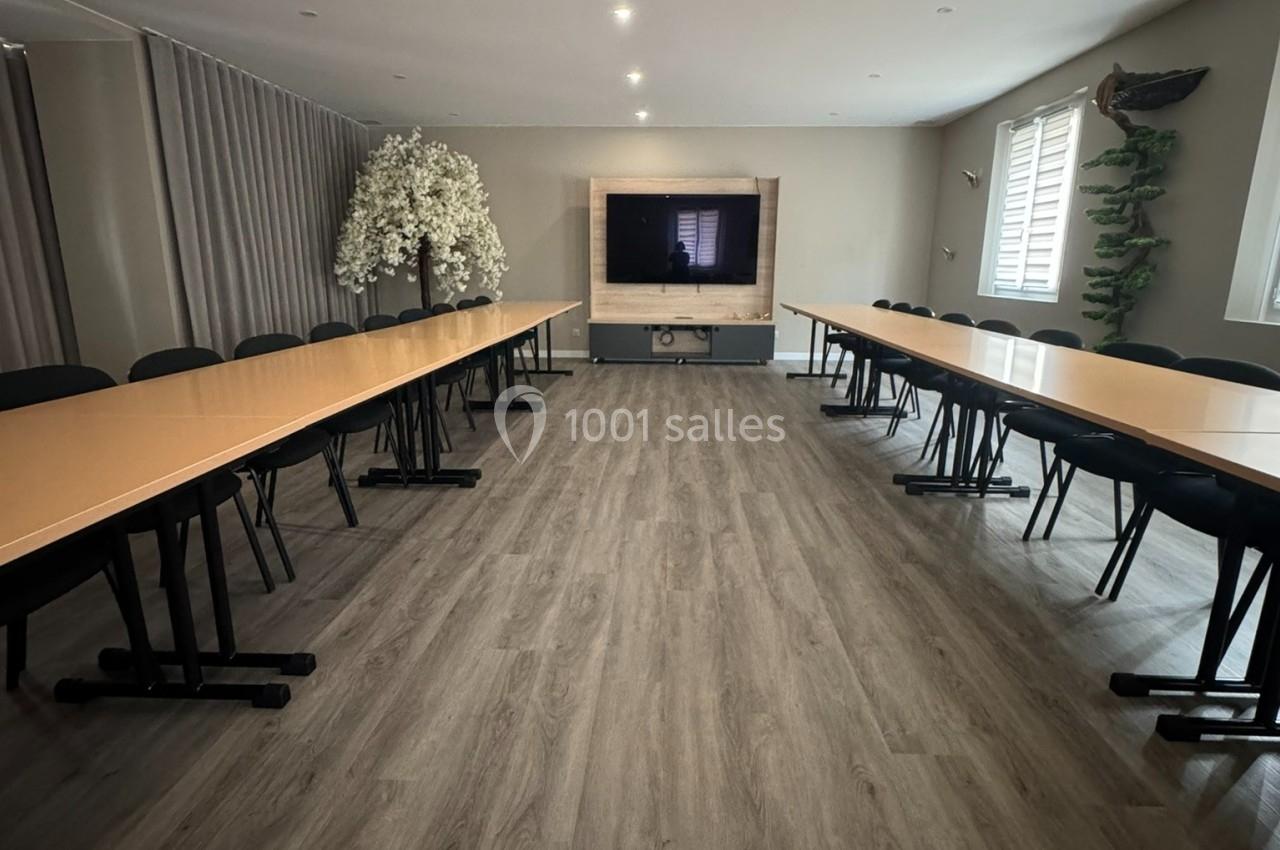 Salle de réunion lumineuse avec deux longues tables en U, écran mural et sol en parquet clair.