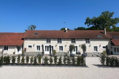 Balancelle en bois rustique sur une pelouse artificielle, avec des bâtiments en pierre et un ciel dégagé en arrière-plan.
